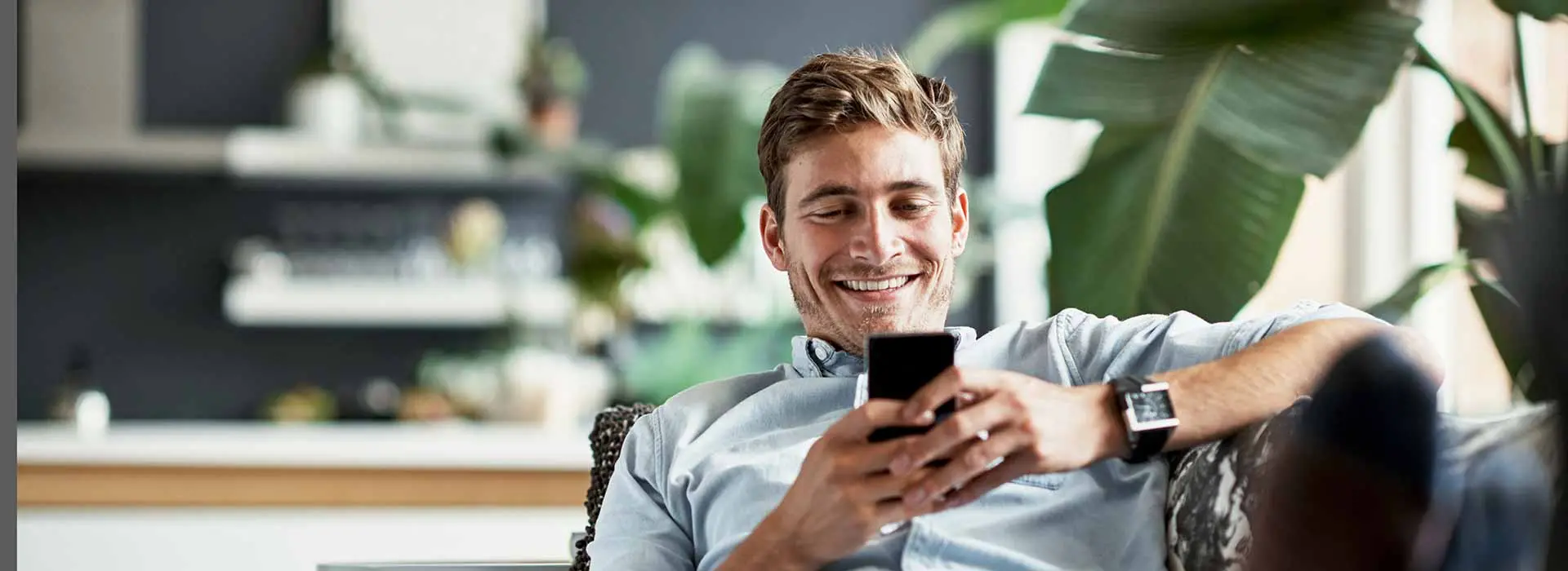 Mann lächelt liegend auf Sofa und tippt auf Handy