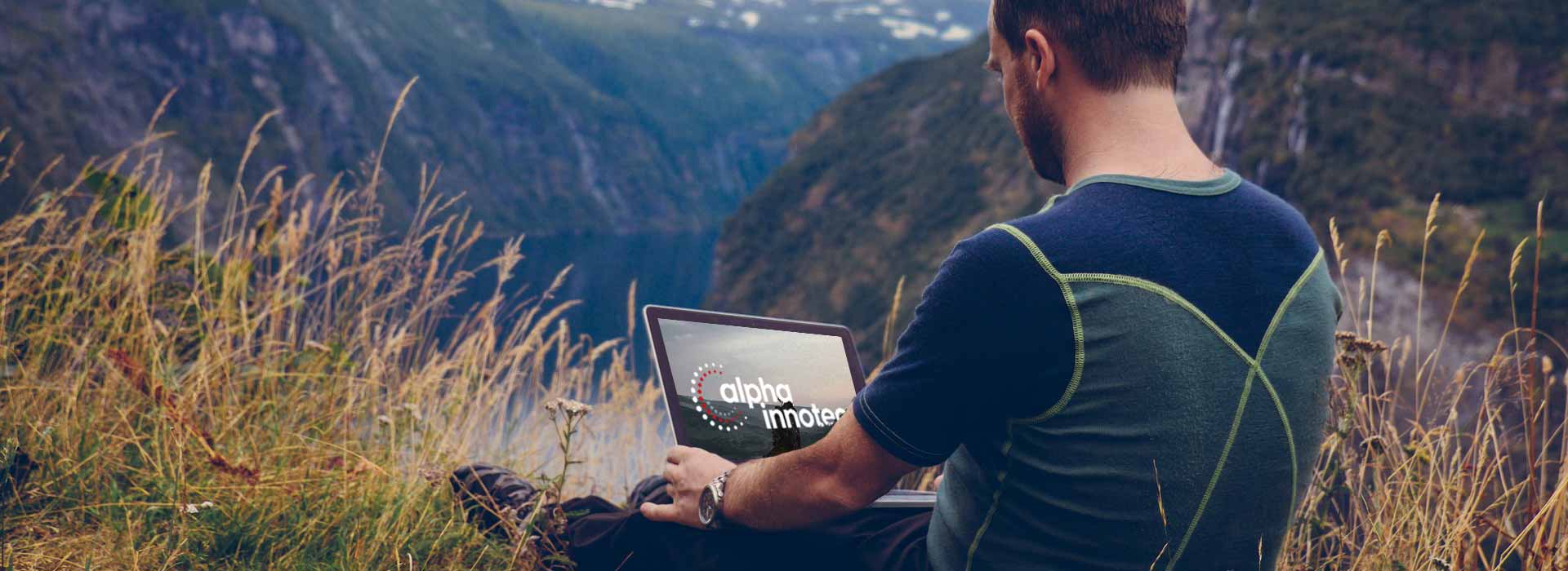 Mann sitzt in Wanderkleidung auf einen Berg mit Laptop
