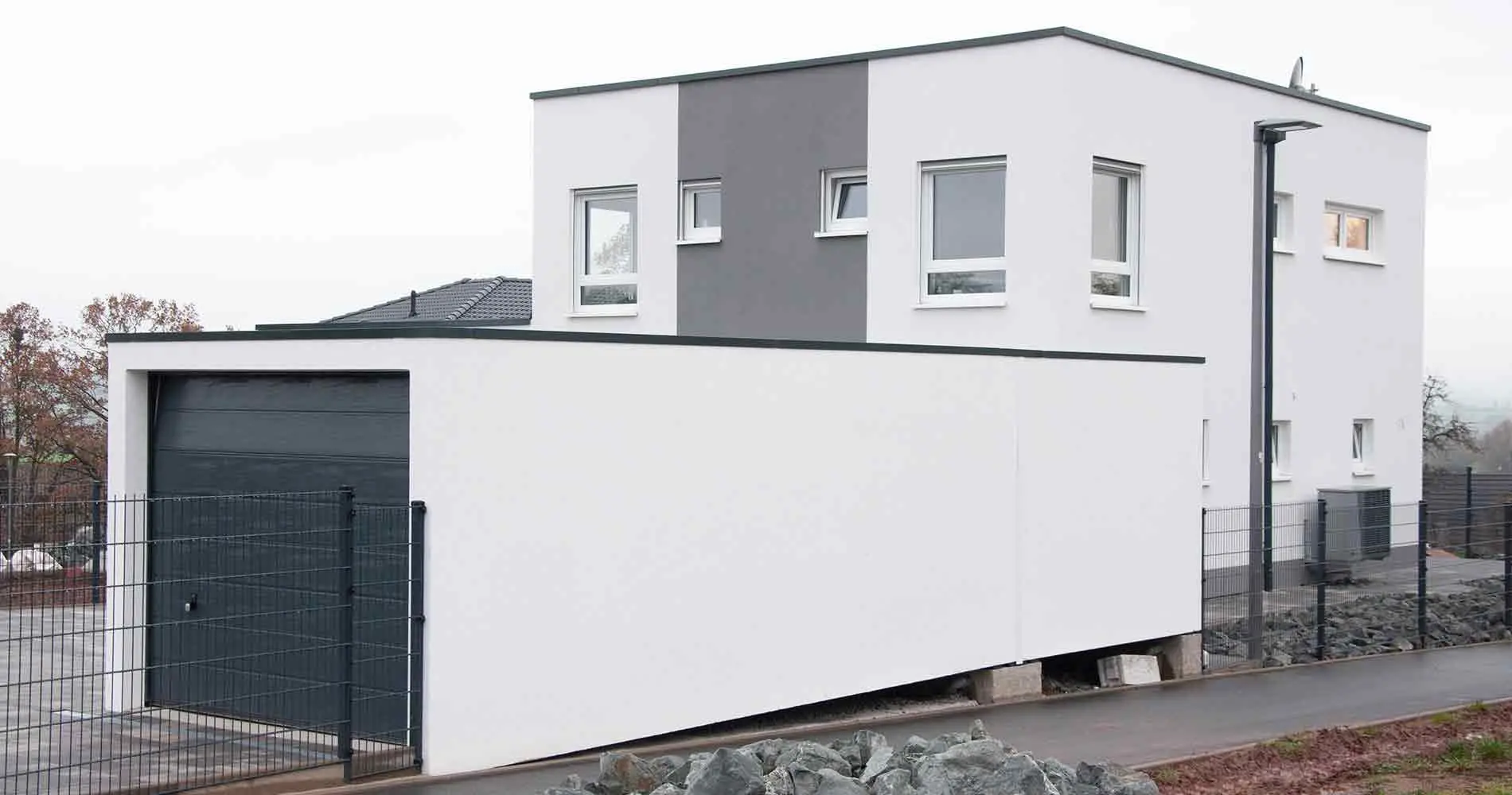 A new building with a flat roof and garage in front stands next to a walkway.