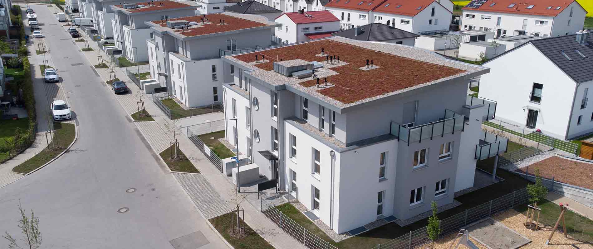 In a modern housing estate, there are several residential buildings with flat roofs next to each other, which were built identically. In the background, you can see different apartment buildings.