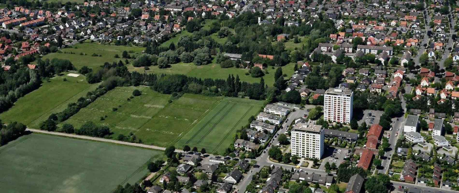 You can see a large residential area with mainly small single-family or multi-family houses and two high-rise buildings. In the middle of the residential area you can see a few larger fields and green area with isolated trees.