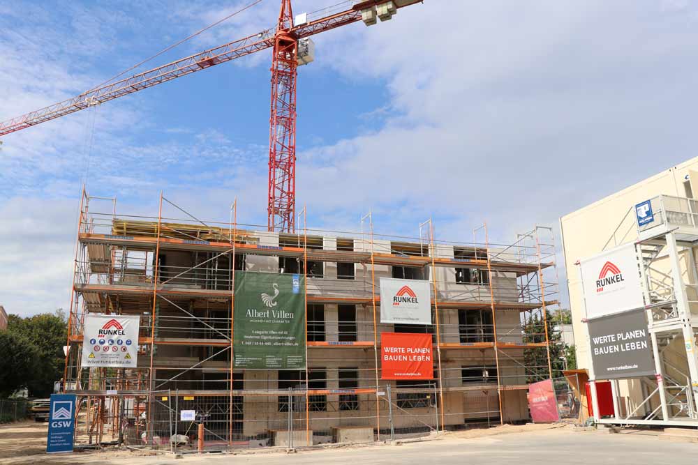 A house stands in front of a crane in the unfinished state, surrounded by scaffolding. On the right side there are containers.