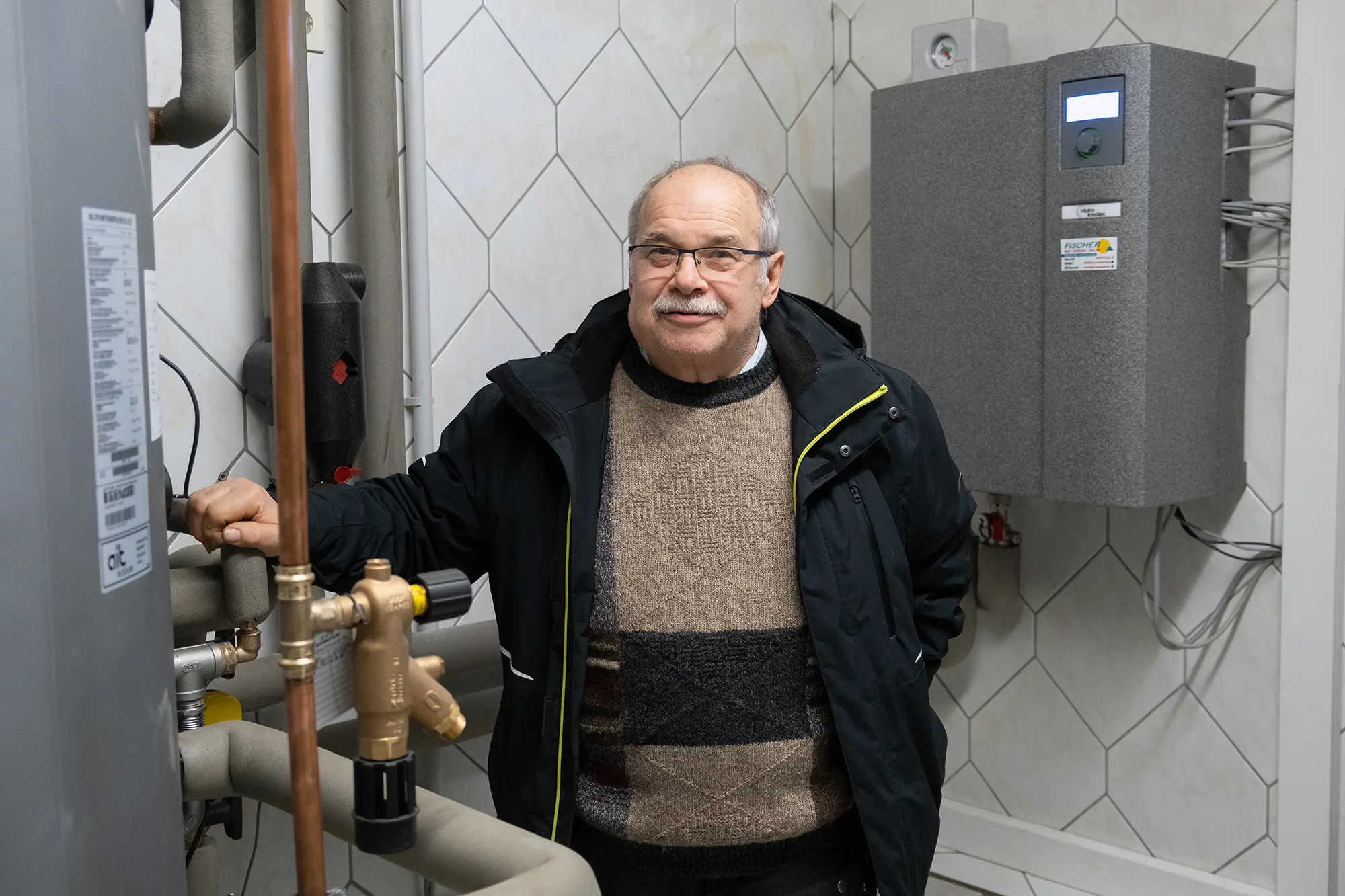 Norbert stands next to the indoor unit of his new alpha innotec heat pump