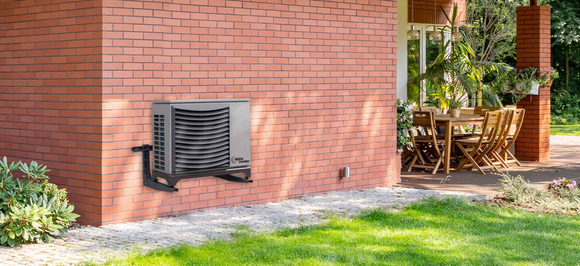 The air/water-heatpump "Jersey" is attached outdoors to a house wall, reaching into a garden.