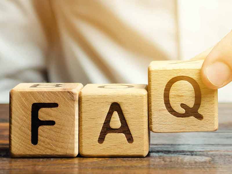 There are three close-up cubes made out of wood with the letters F,A and Q, one letter each cube. A person puts the last cube with the letter Q down to spell the word FAQ. 