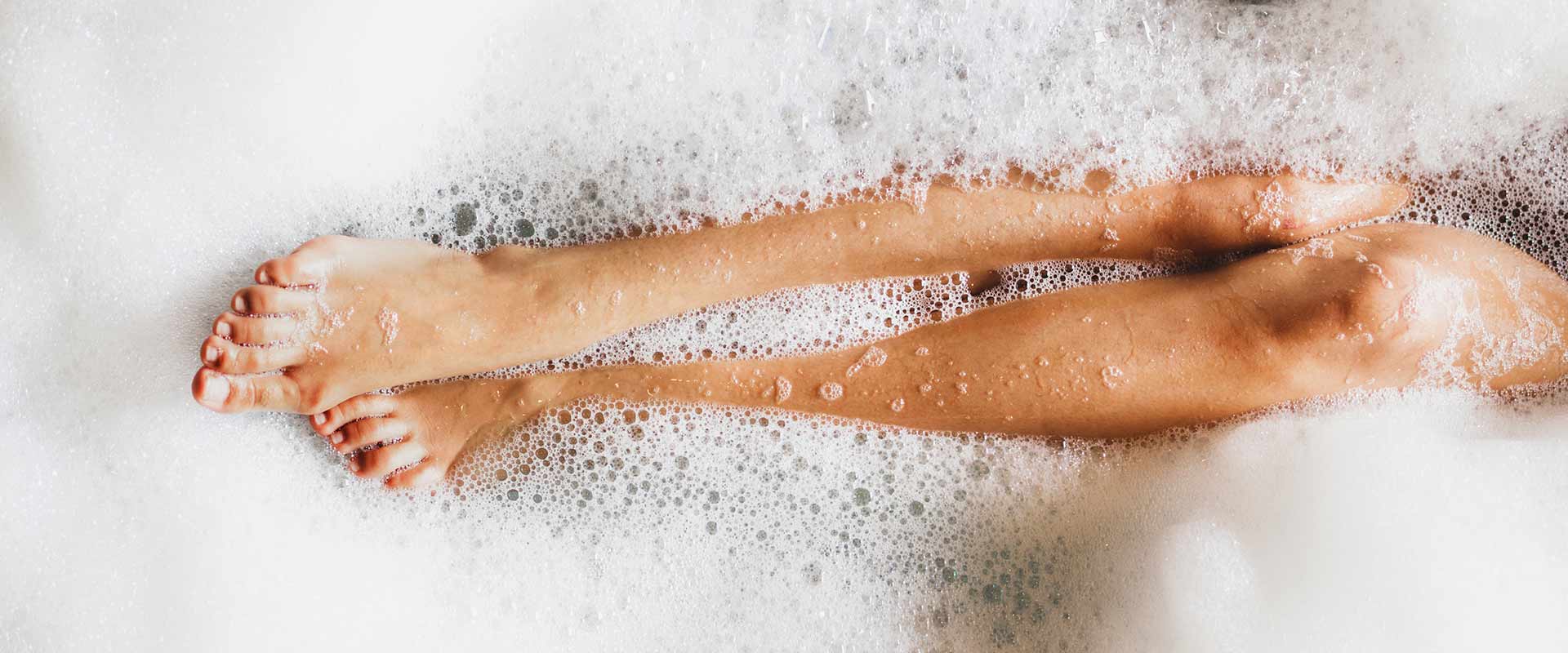 The legs of a woman peek out from a bubble bath and the bubbles surround her completely.